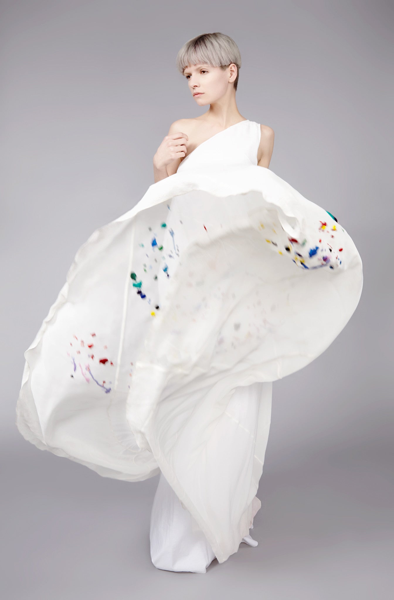 Embroidered one shoulder long dress sewn with bias cut sections of fabric to wrap around the body, allowing a slim top part and extra wide hemline. Embellished by beautiful multicoloured paint splash embellishments.