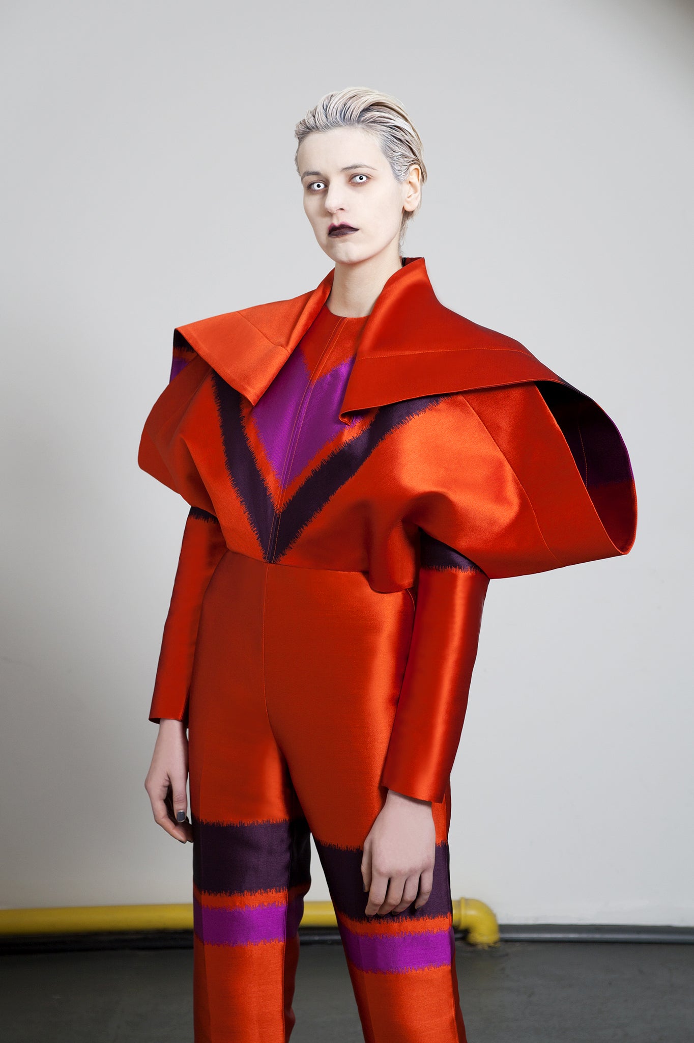 Channel the original David Bowie 'Starman' with this statement all-in-one. Featuring an oversized ‘winged’ shape extending down from the shoulder. A sister to the “Boeing” dress, this piece is draped with a wrap at the shoulder point. The fitted body and slim line leg further accentuates the scale of the outstretched wing.